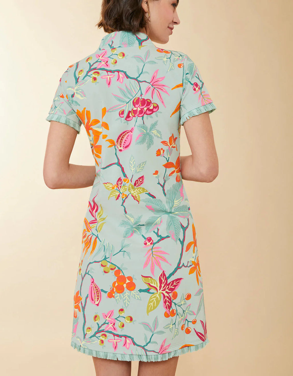 A woman wearing a short-sleeve cheongsam-style dress with a light mint green base and a colorful floral print, shown from the back against a solid beige background.