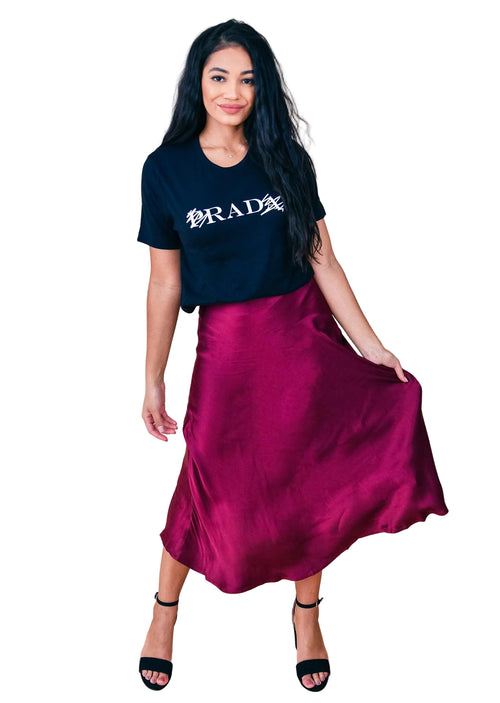 Woman wearing a black Prada t-shirt and burgundy satin skirt on a beige background