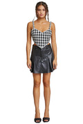 Woman wearing a black and white houndstooth patterned top and black leather skirt against a plain background