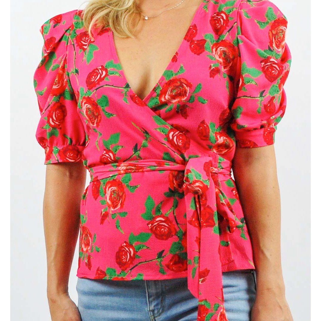 Woman wearing a pink floral wrap top with blue jeans on a white background