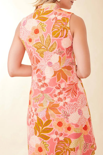 A woman wearing a sleeveless coral pink dress with a yellow and orange floral pattern, shown from the back against a light beige background.